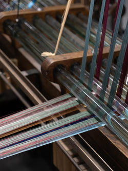Fils de chaîne colorés passant dans des guides en verre sur métier à tisser