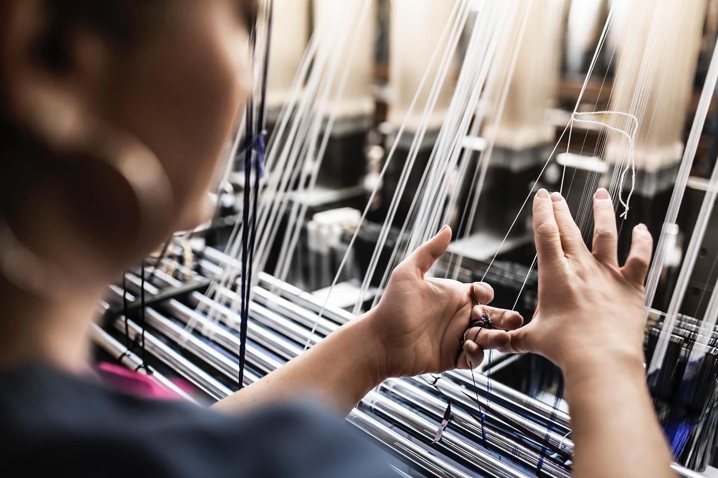 Mains d'artisan ajustant les fils de chaîne blancs sur un métier à tisser