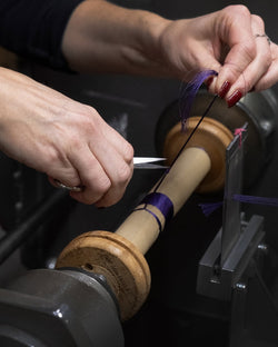 Mains d'artisane coupant un fil violet sur une bobine en bois