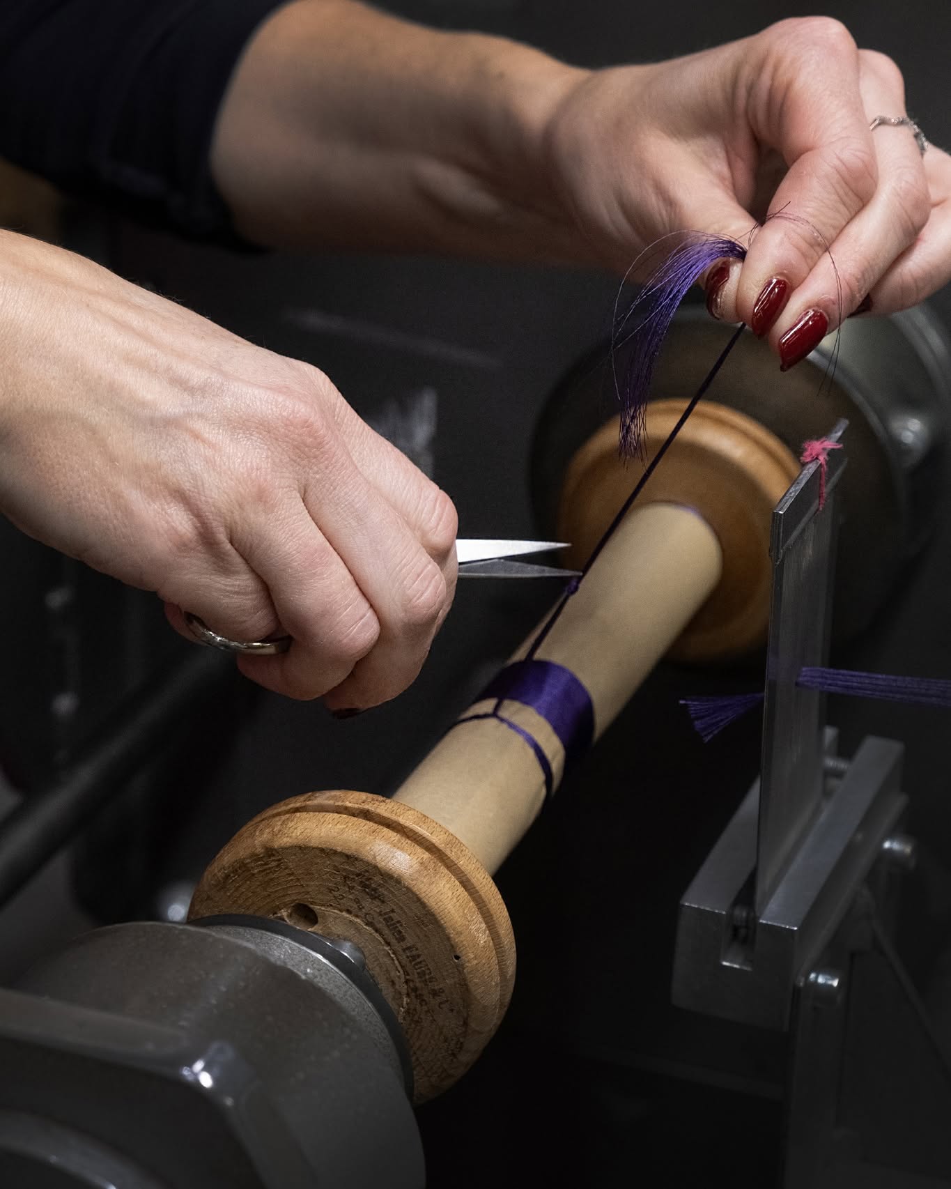 Mains d'artisane coupant un fil violet sur une bobine en bois